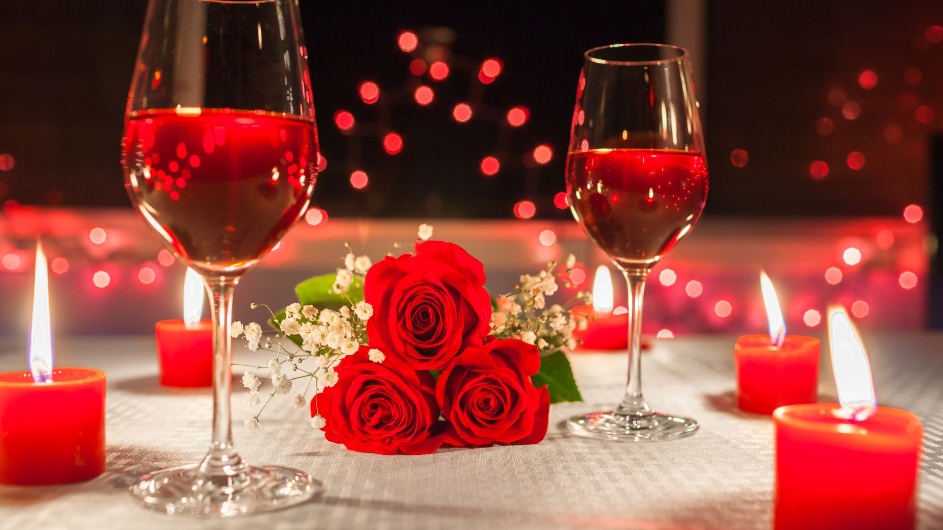 Imagem de uma mesa com velas, flores e duas taças de vinho, como se fosse em um jantar