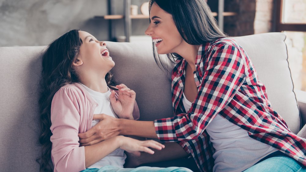 Roman Samborskyi / Shutterstock.com Tia brincando com a sobrinha no sofá. Ambas estão rindo
