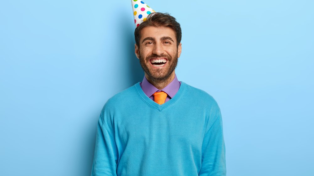 Homem sorrindo com chapéu de aniversário.