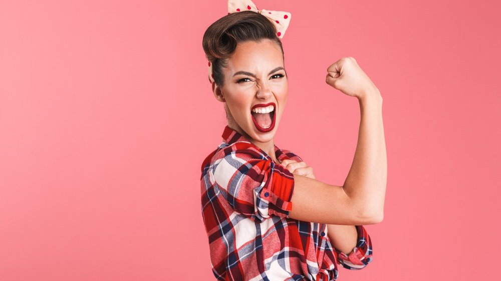 Mulher sorrindo e fazendo pose de força com fundo rosa