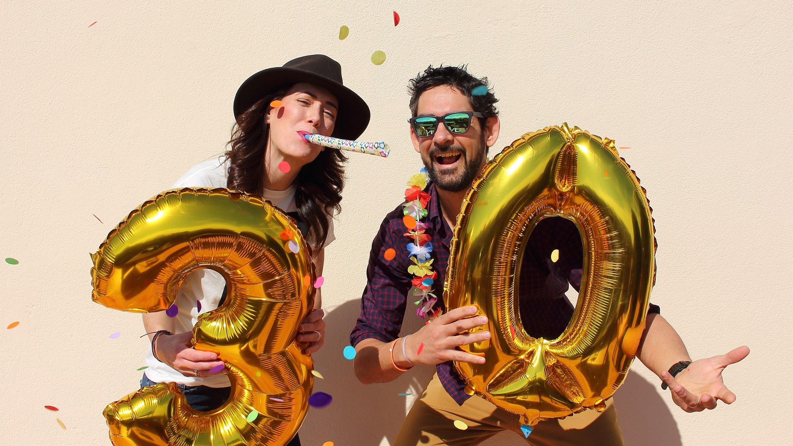 Homem e mulher segurando balão dos números três e zero, comemorando e sorrindo