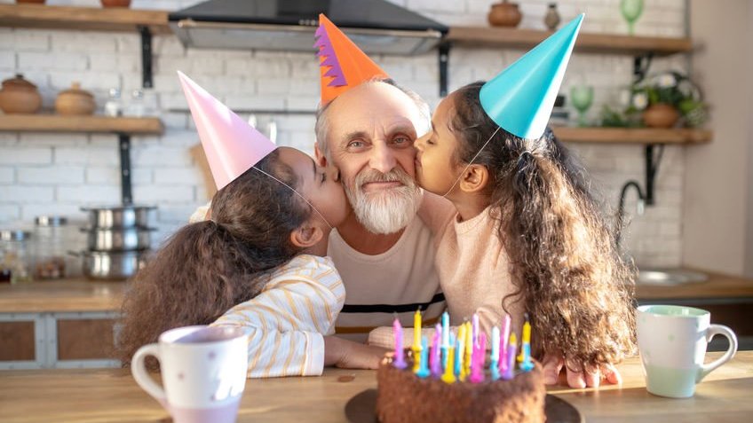Duas meninas beijando um homem mais velho nas bochechas comemorando aniversário