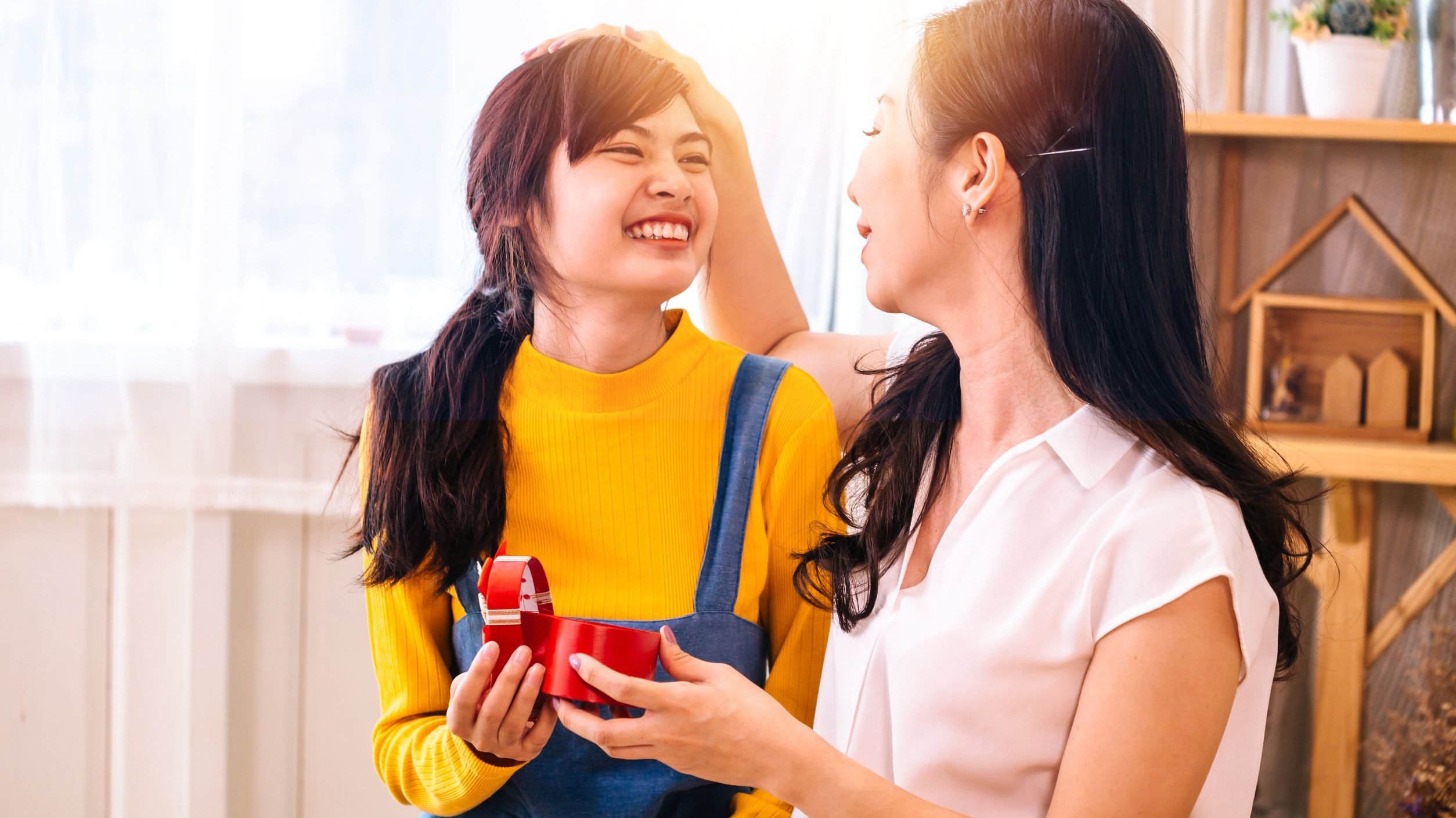 Duas mulheres sentadas no sofá sorrindo e segurando um presente de aniversário.