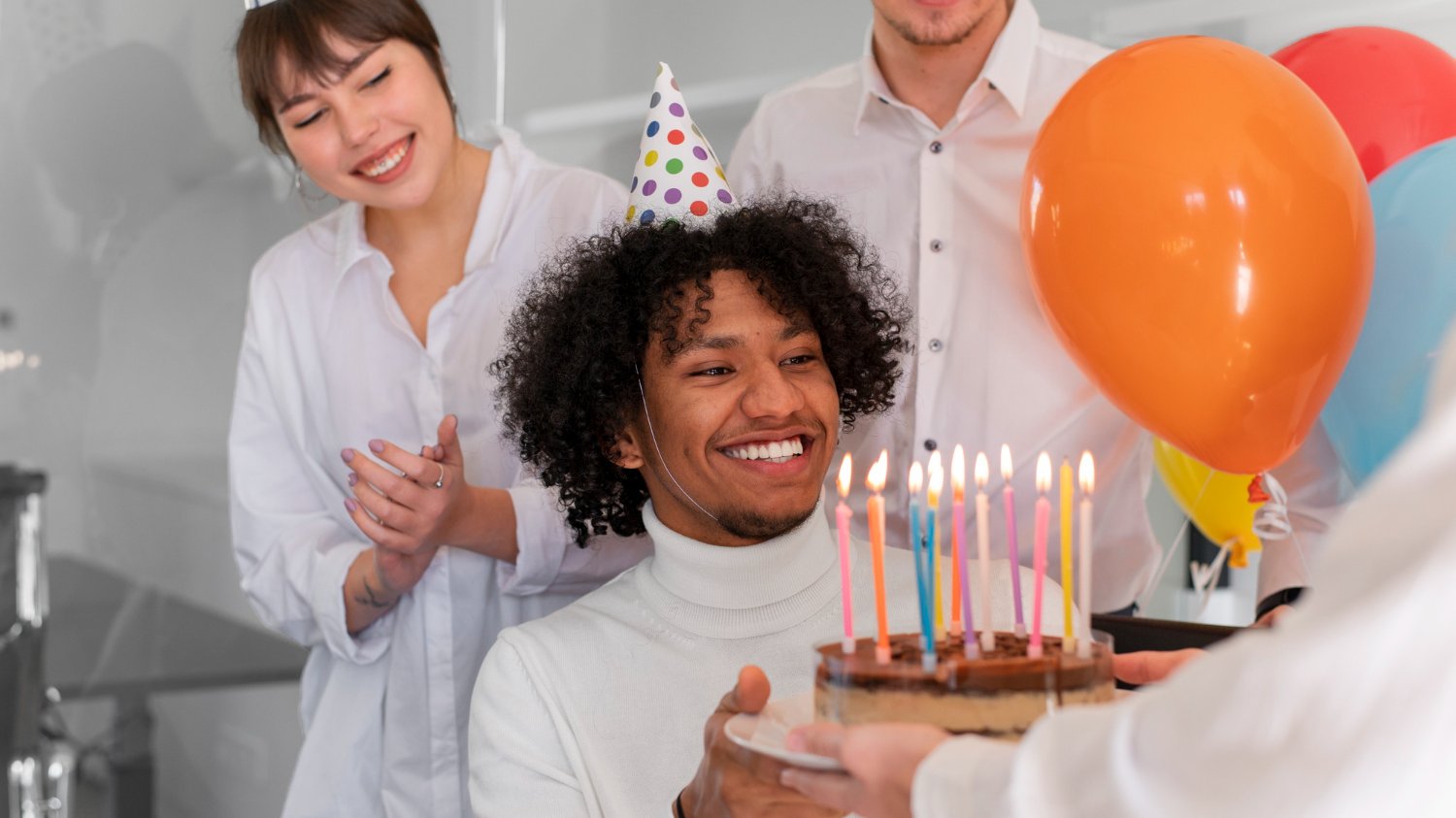 Homem negro ganhando bolo de aniversário, cercado de pessoas de diversas etnias.