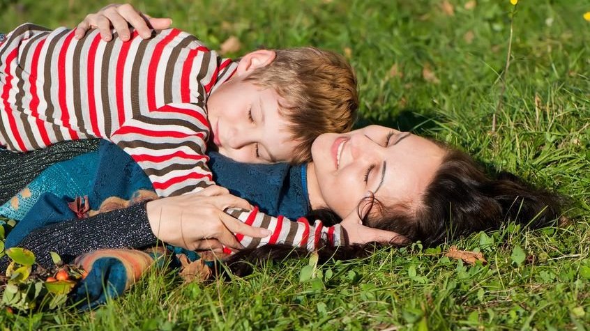 Mãe e filho deitados na grama verde.