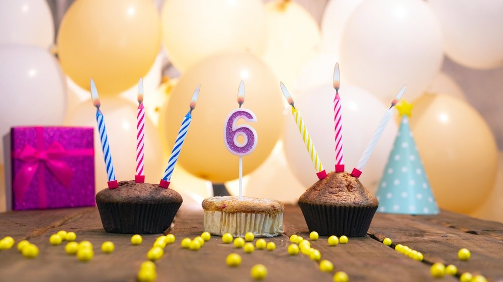 Mesa enfeitada com balões e chapéus de aniversário com um cupcakes ao centro e uma vela de número 6 em cima de um deles.