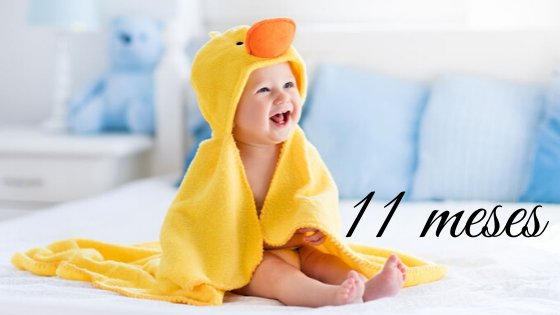 Bebê sentado na cama com toalha de patinho sorrindo escrito 11 meses