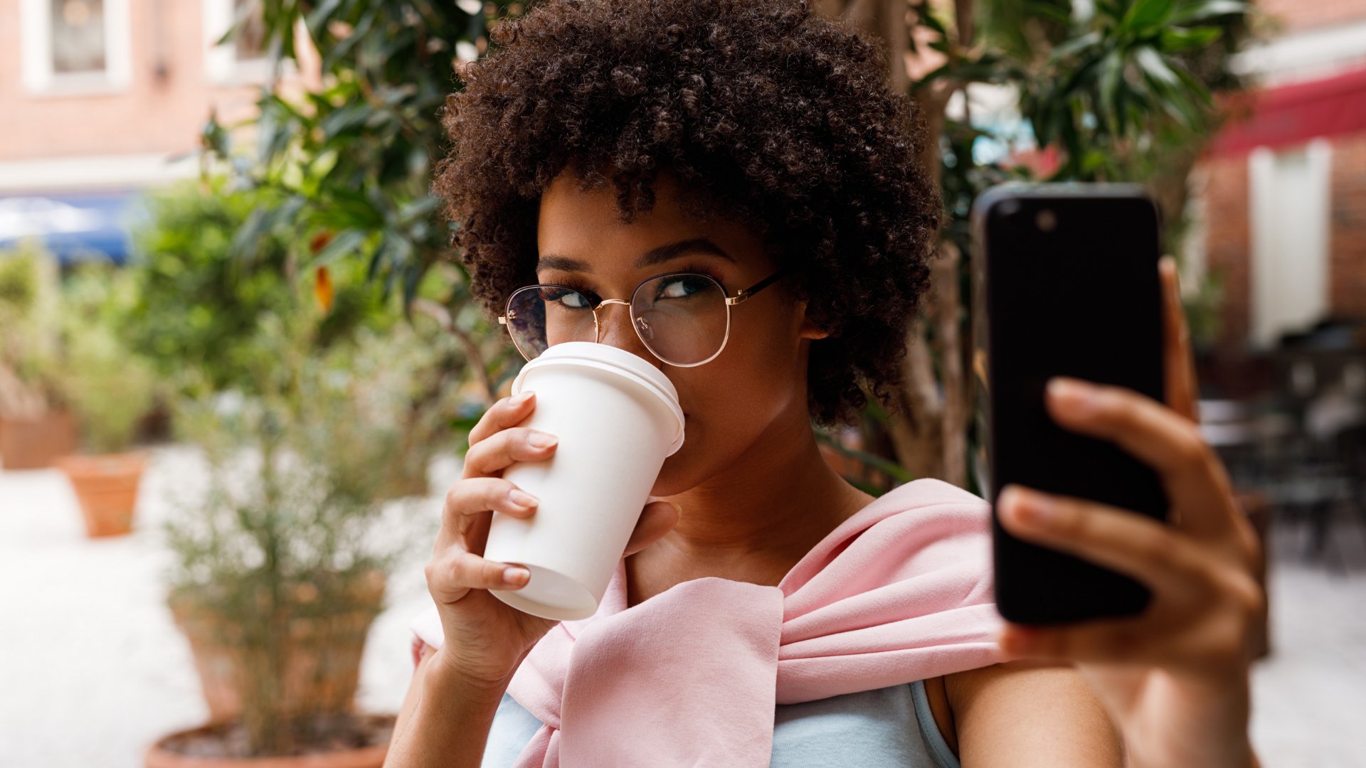 Mulher segurando celular enquanto toma café