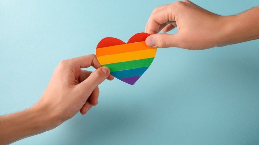 Duas mãos segurando coração com as cores da bandeira LGBT