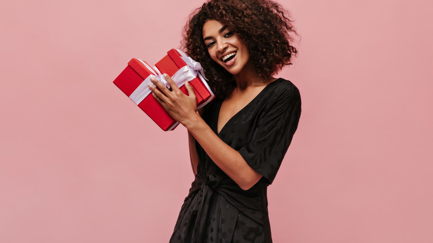 Mulher negra segurando duas caixas de presente enquanto sorri