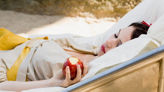Mulher vestida de branca de neve, adormecida enquanto segura uma maçã