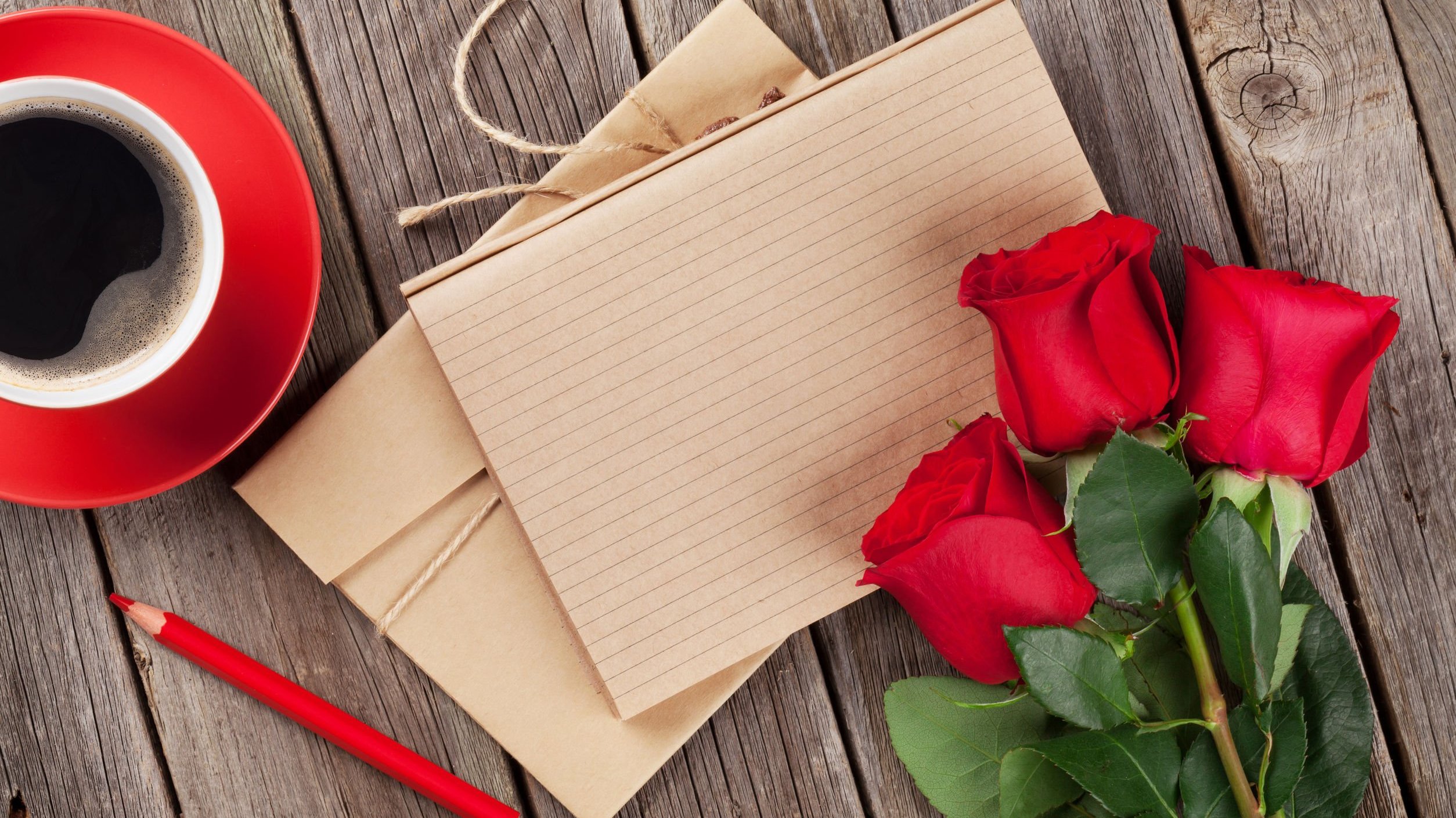 Papeis de carta ao lado de um buquê de rosas e uma xícara de café.