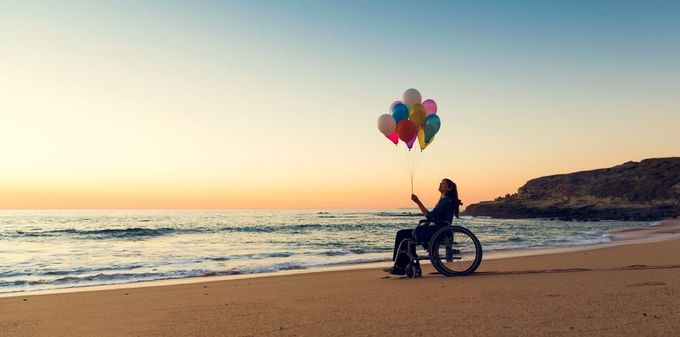 Mulher de cadeira de rodas em praia segurando balões