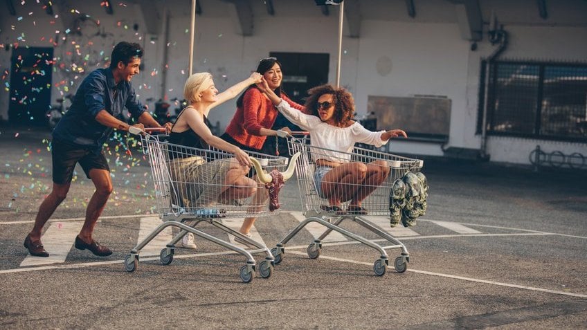 Quatro pessoas no estacionamento de supermercado brincando com o carrinho de compras