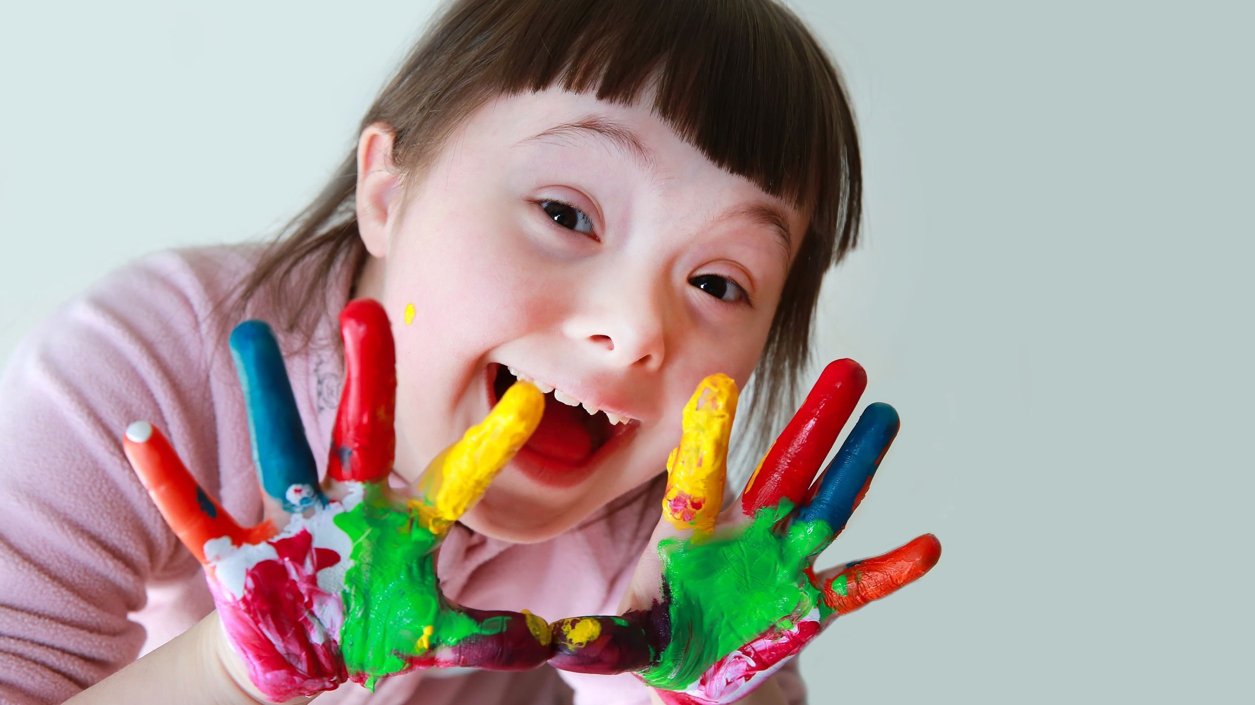 Garota com Síndrome de Down de mãos sujas de tintas coloridas sorrindo