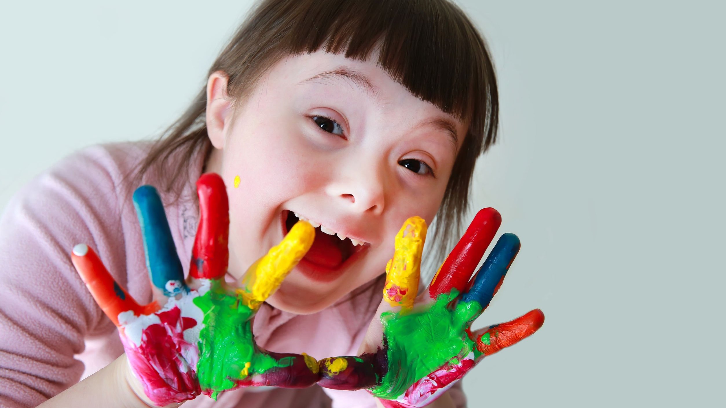 123RF Garota com Síndrome de Down de mãos sujas de tintas coloridas sorrindo