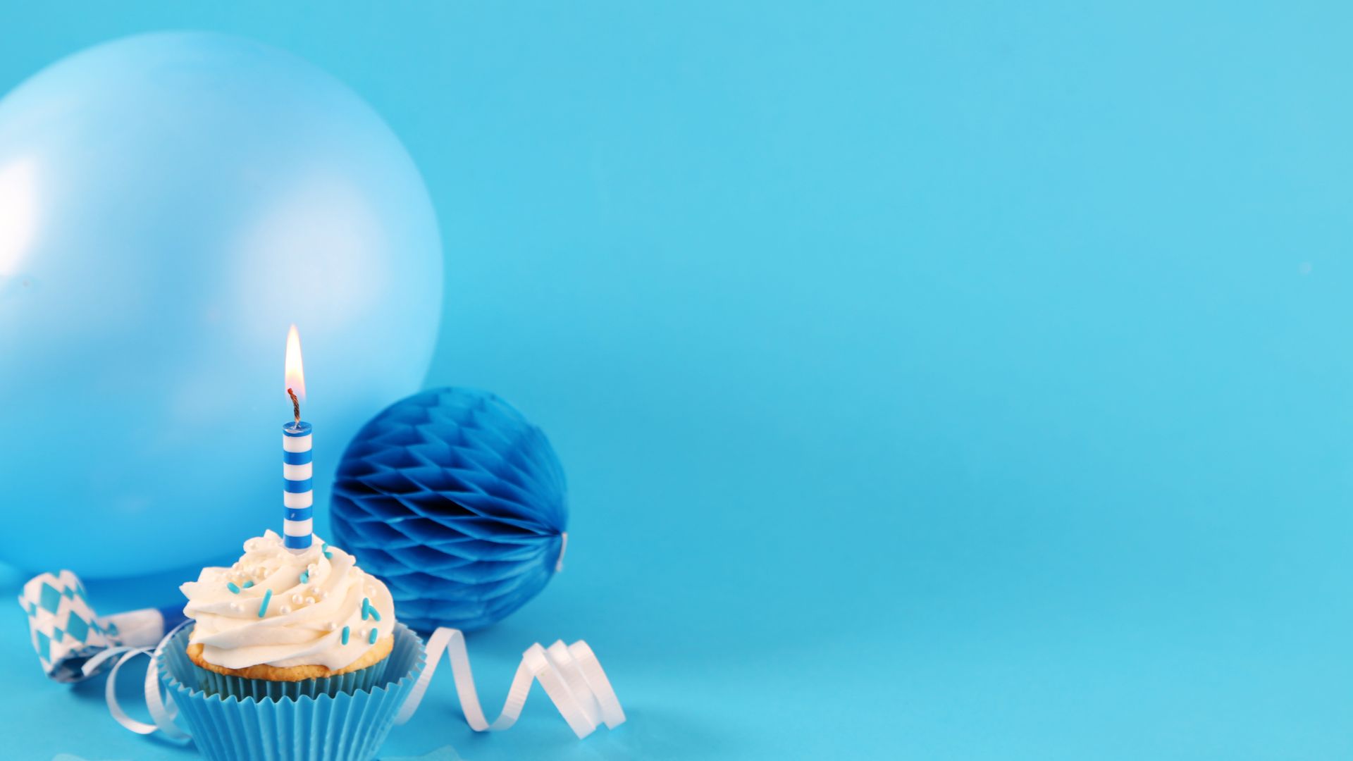 Imagem de um balão azul, fita remetendo a aniversário e um cupcake com uma vela no topo