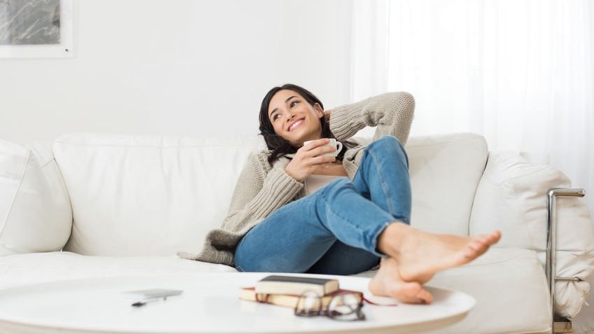 Mulher sentada no sofá segurando xícara com expressão de tranquilidade