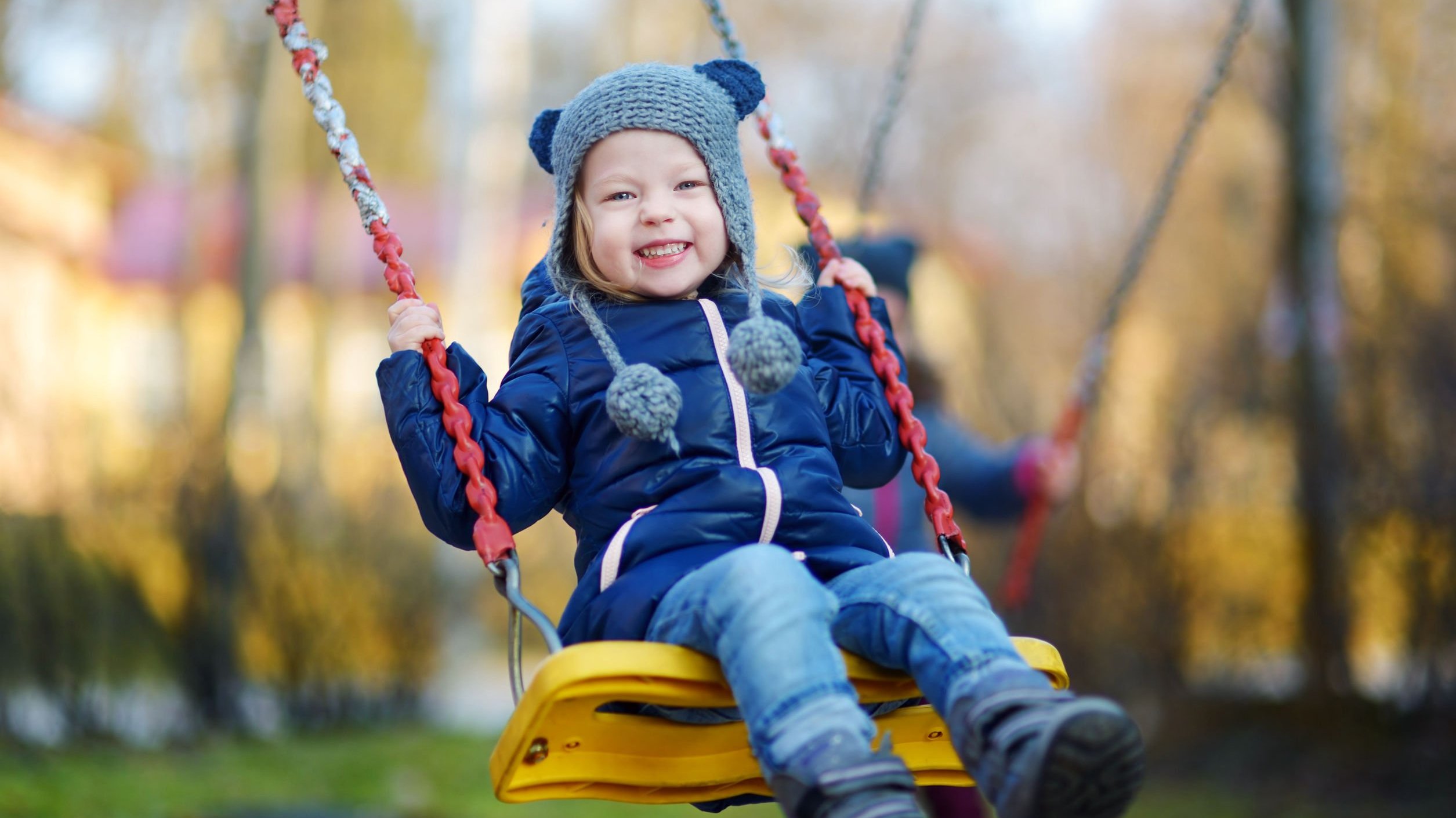 Criança menina com roupas de frio sorrindo enquanto brinca em um balanço