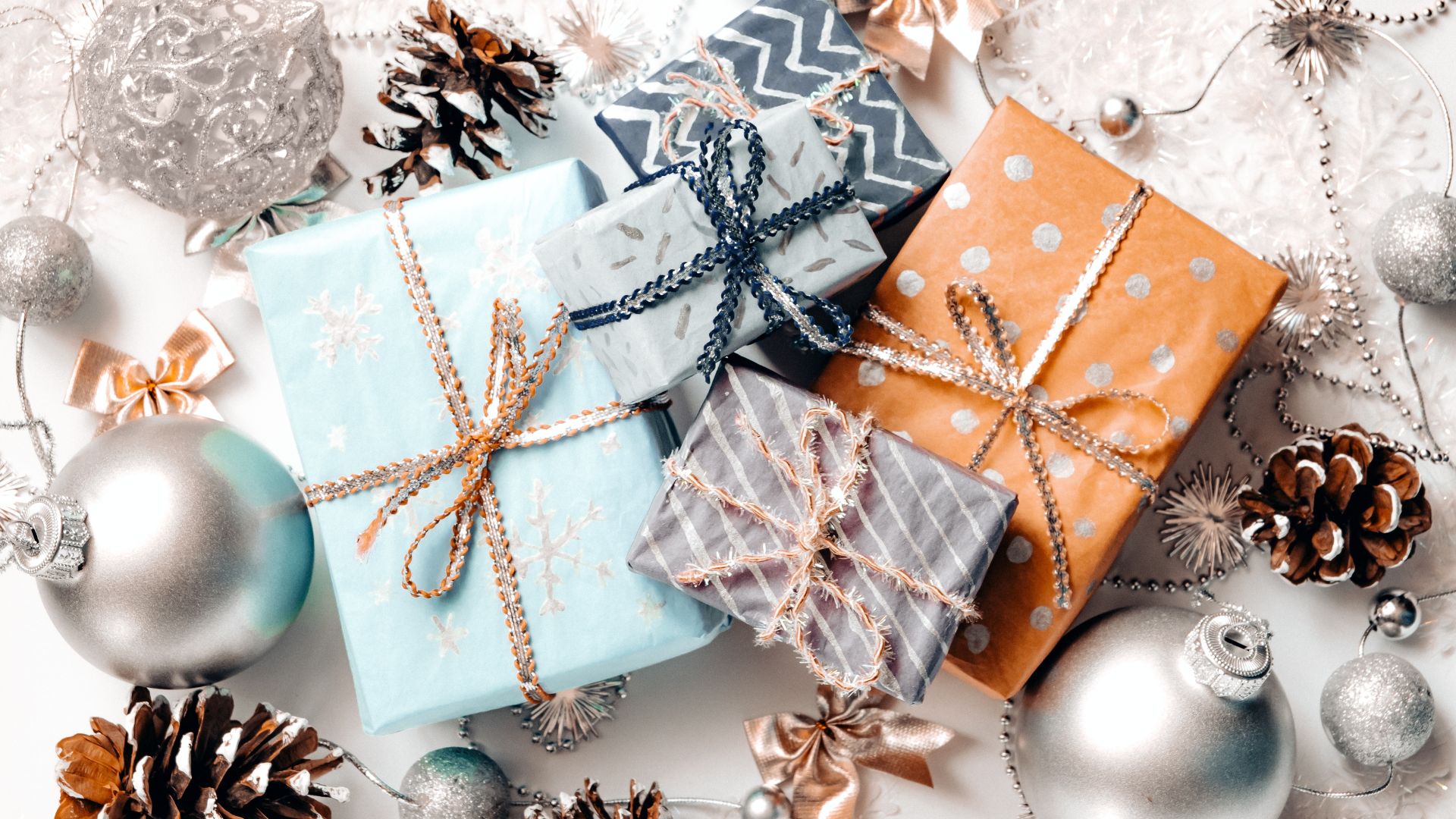 Imagem de fundo branco com vários elementos natalinos como vaixas de presentes, bolas de árvore de natal, pinhas e laços.