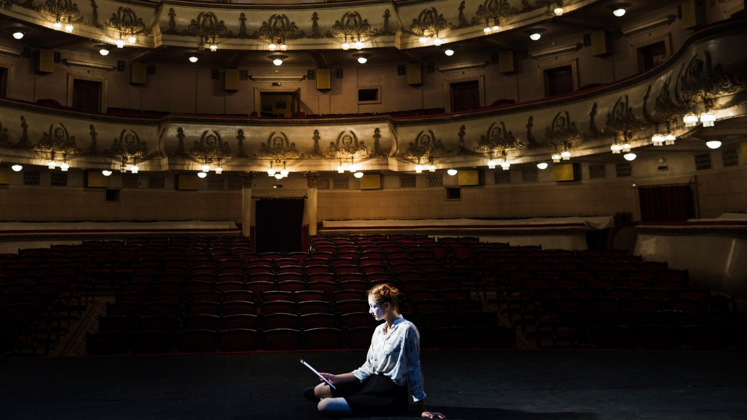 Mulher em cima do palco e ao fundo, as poltronas do teatro