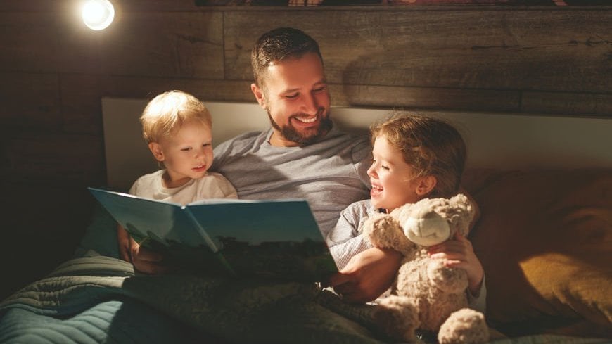 Pai lê um livro para os filhos na cama