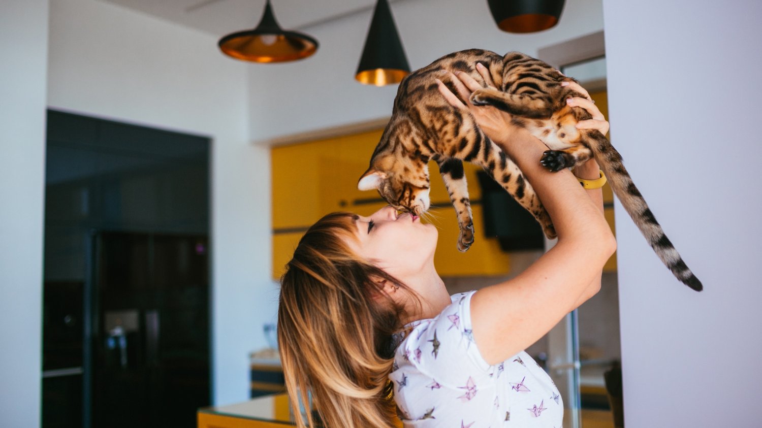 Mulher branca com cabelos claros beijando seu gato tigrado