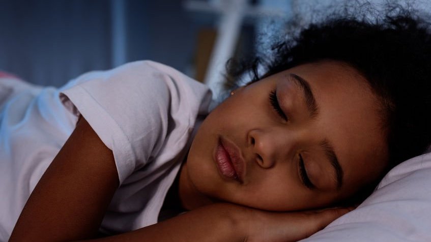 Criança negra dormindo na cama em casa.