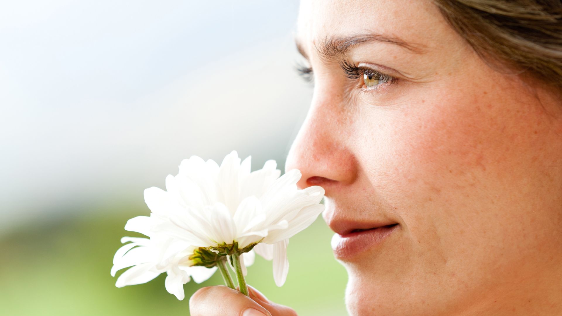 Imagem de uma mulher cheirando uma flor e olhando para o horizonte