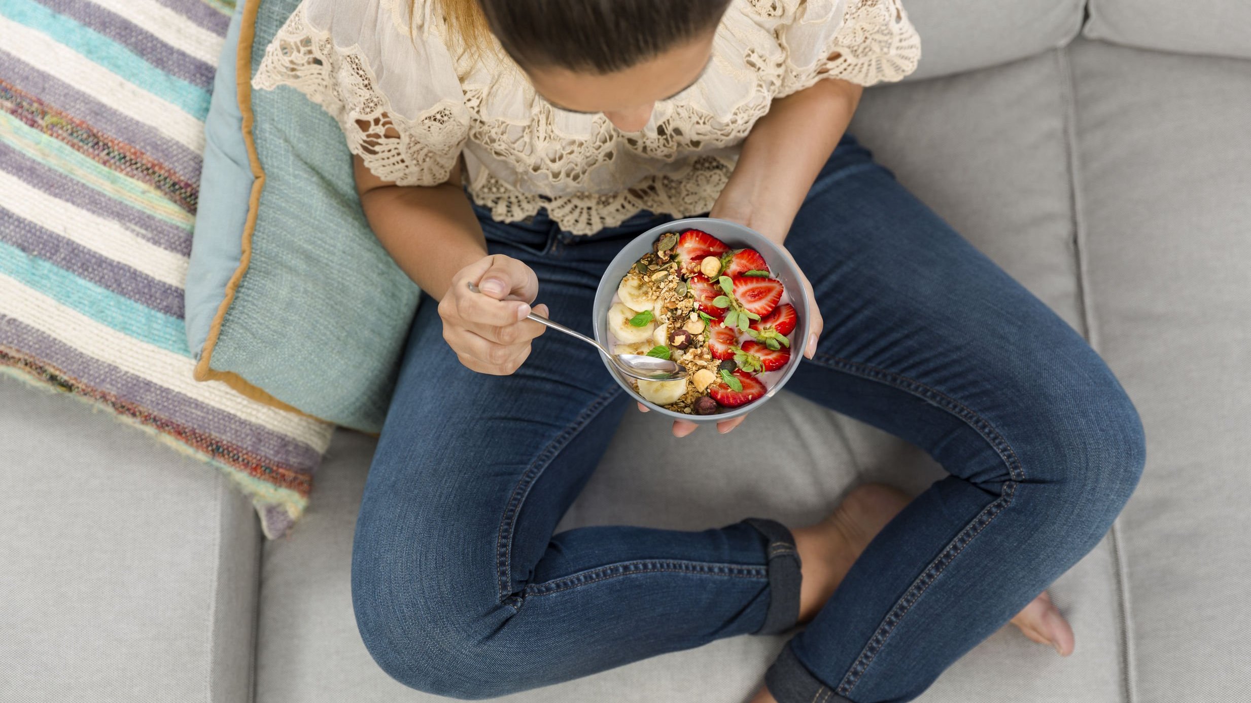 Mulher sentada no sofá comendo um pote de frutas