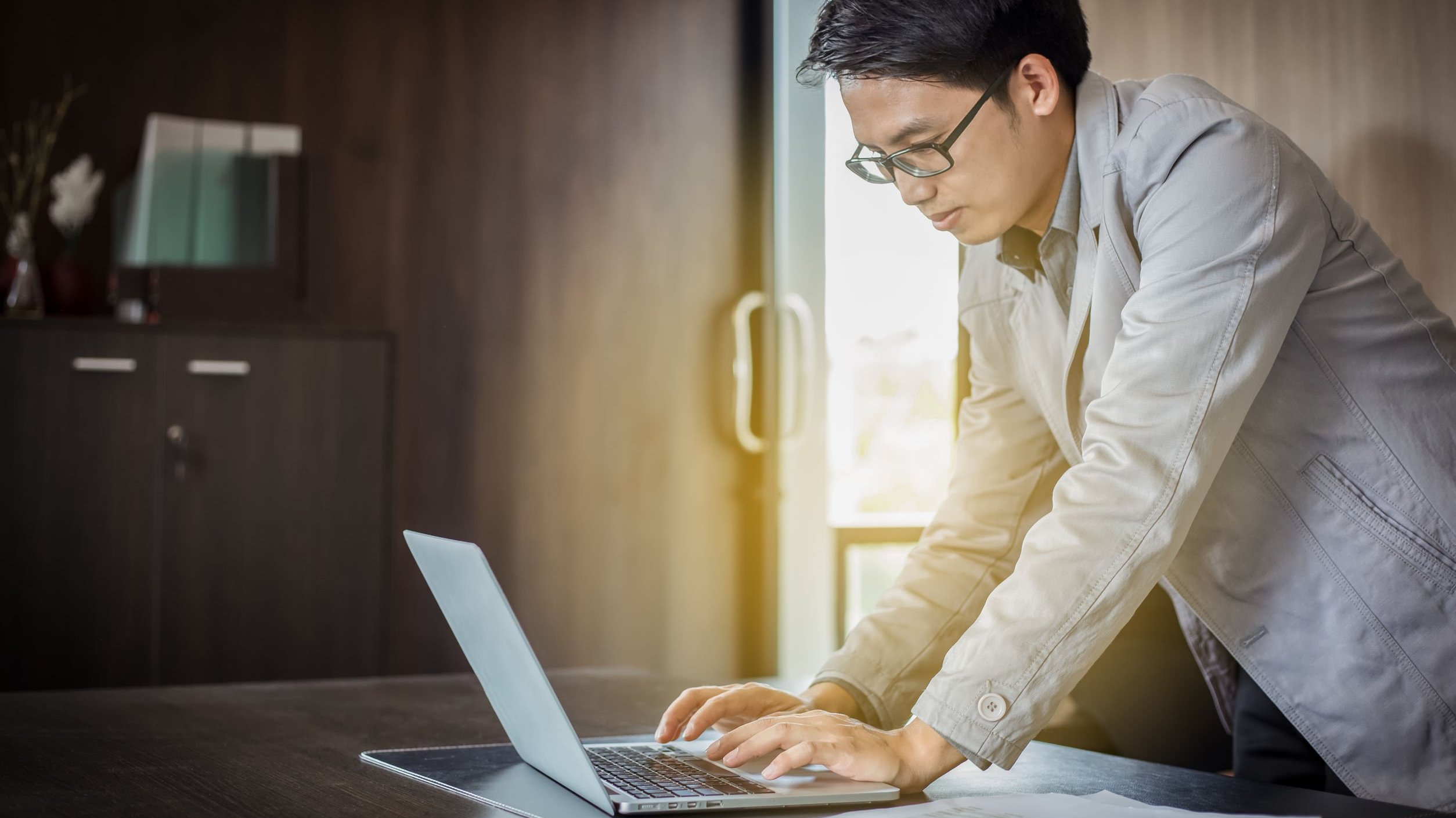 Homem de pé mexe em computador que está sobre uma mesa