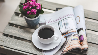 Café em cima de revistas com um vaso de flor ao lado