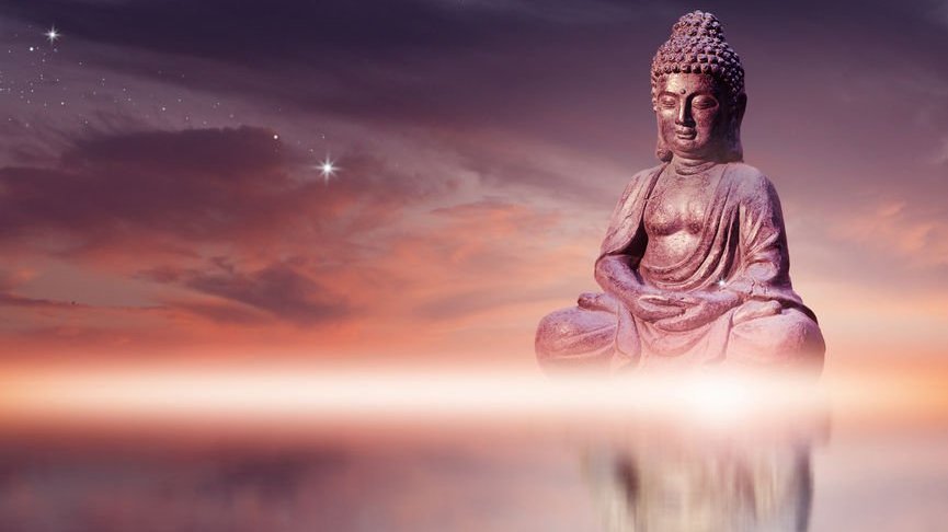 Estátua de Buda sentado em pose de meditação contra o céu do sol com nuvens de tons dourados.