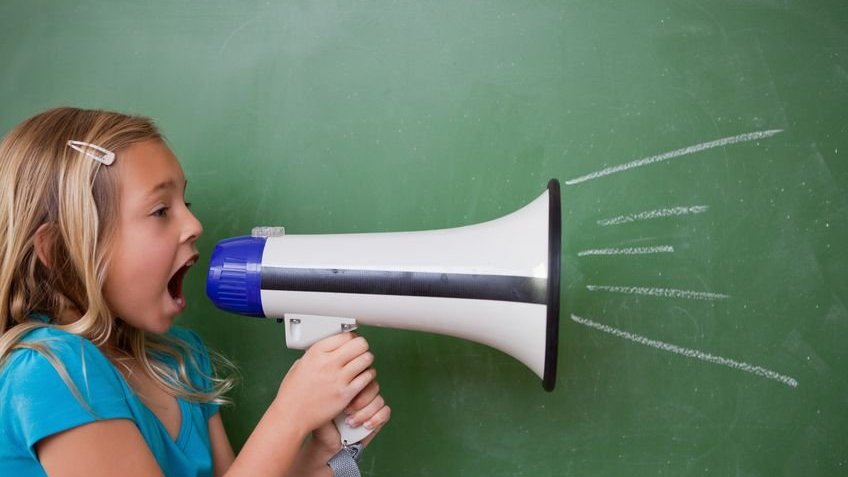 Uma menina gritando em um megafone na frente do quadro-negro