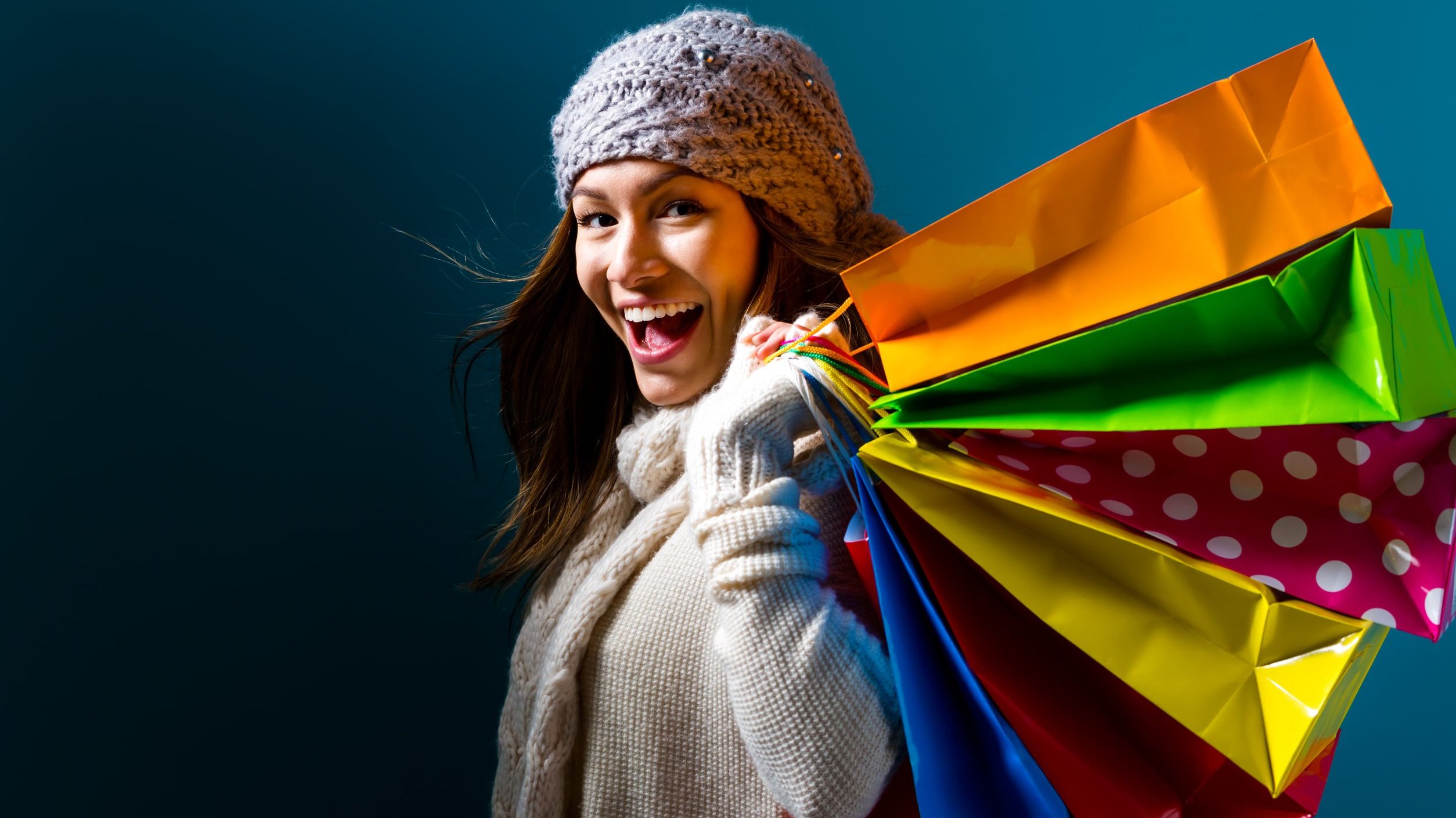 Mulher com roupas de frio sorrindo e segurando sacolas de compras
