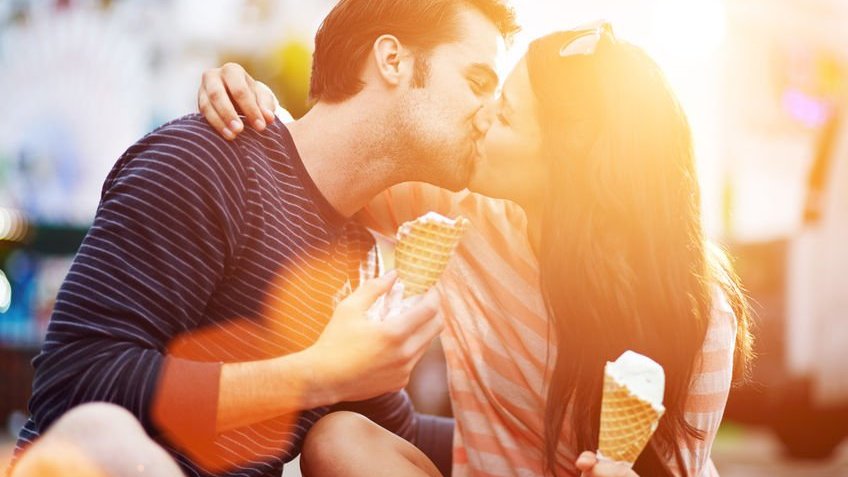 Homem e mulher se beijando, enquanto cada um segura uma casquinha de sorvete.