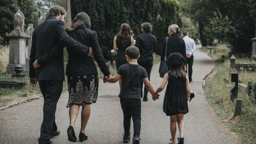 Família andando com roupas pretas em cemitério