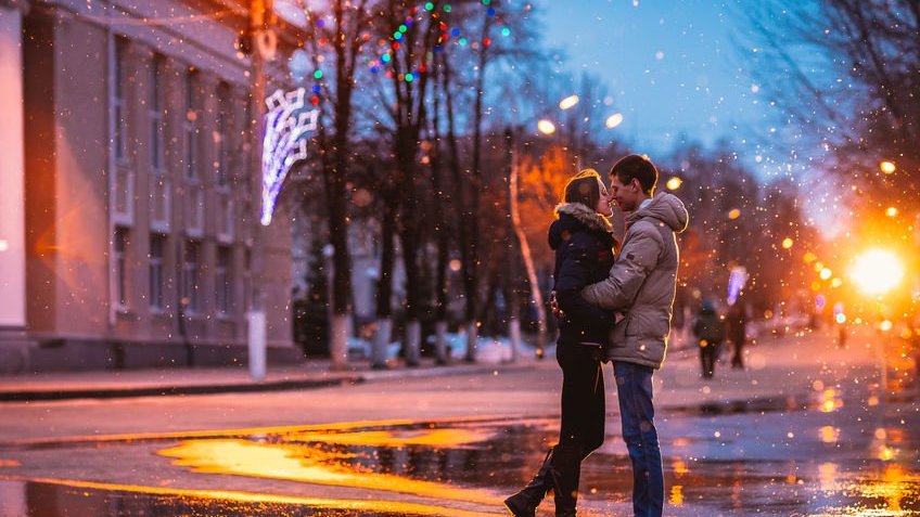 Casal apaixonado beijando na neve na rua da cidade à noite.