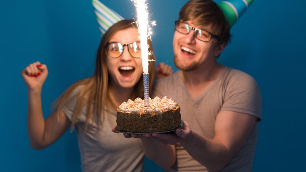 Homem e mulher sorrindo para o bolo com uma vela soltando faíscas