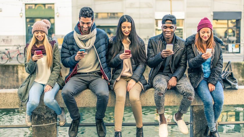 Amigos encostados em muro todos mexendo em seus celulares