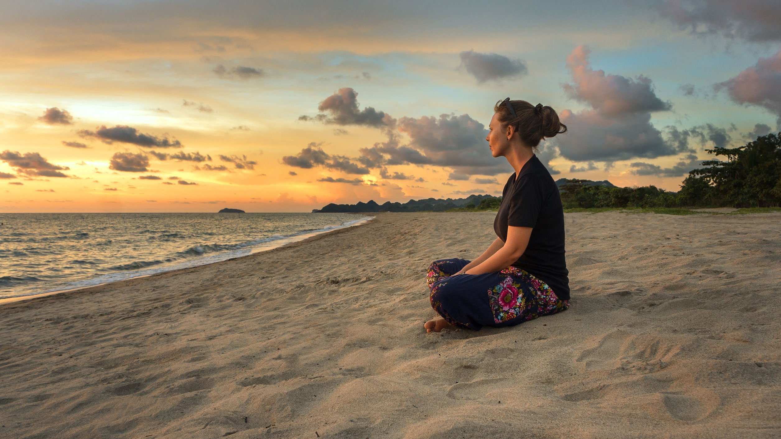 Mulher sentada na areia da praia olhando para o mar