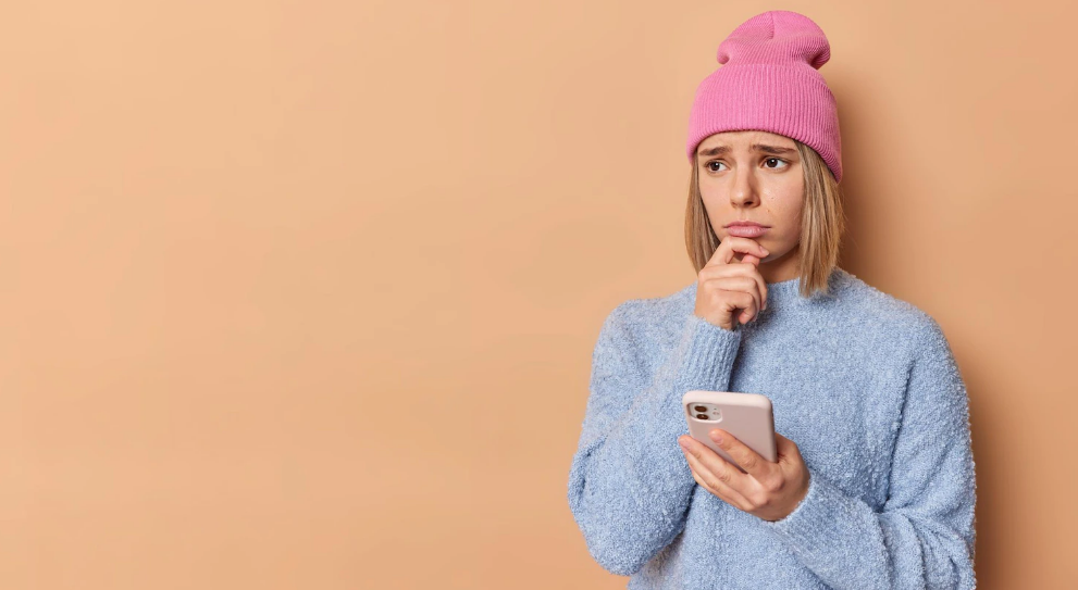 Mulher segurando o celular com expressão de tristeza.