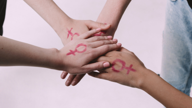 Mulheres com as mãos umas em cima das outras com o símbolo feminino desenhado na mão