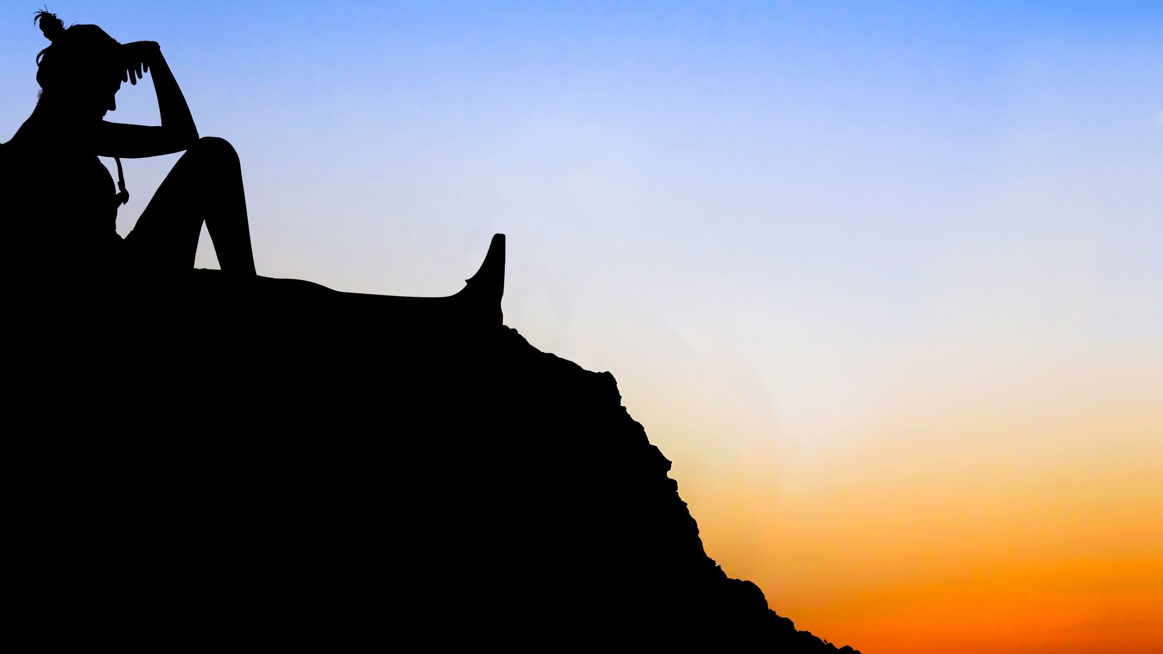 Silhueta de mulher sentada num morro durante o pôr-do-sol.