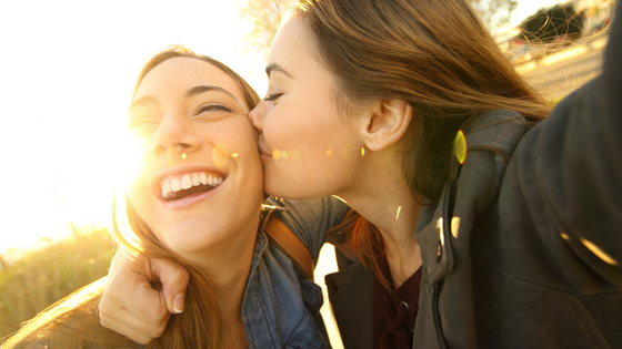 Uma mulher sorrindo enquanto a outra dá um beijo na bochecha
