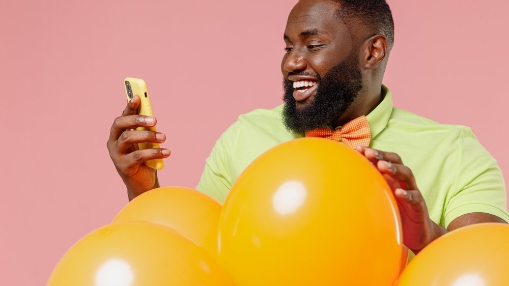 Homem feliz, segurando balões e olhando para o celular.