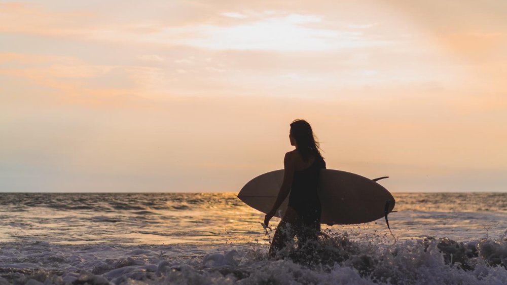 Mulher segurando uma prancha de surf andando pelo mar