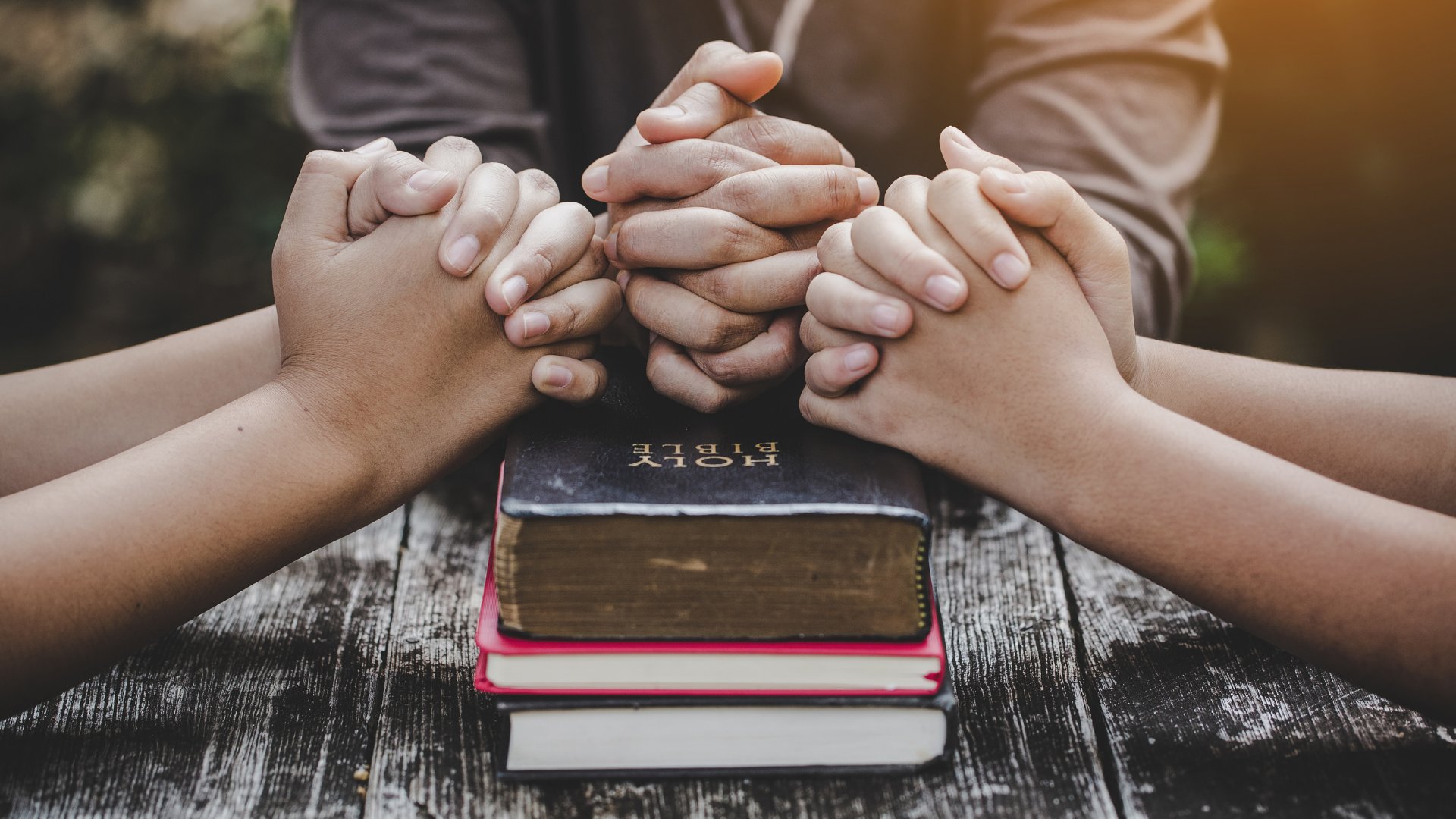 Grupo de oração com as mão juntas sobre uma bíblia
