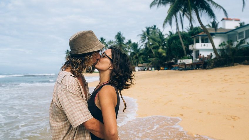 Homem e mulher brancos se beijando na praia.