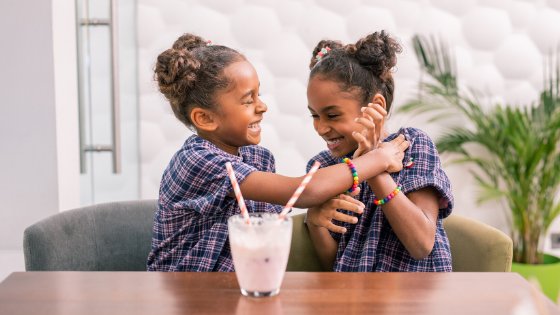 Duas irmãs sorrindo sentadas em uma mesa com um milkshake